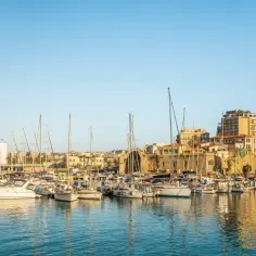 Port w Heraklionie, gdzie cumują jachty, z widokiem na kamienne mury i budynki starego miasta.