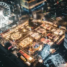 Nocny jarmark bożonarodzeniowy Katowice tętni życiem. Widać karuzelę, diabelski młyn i liczne stoiska rozświetlone tysiącami lampek.