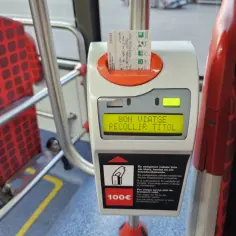 Bilety metro Barcelona w automacie. Na ekranie "BON VIATGE RECOLLIR TITOL". W tle czerwone siedzenia.