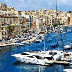 Malta co zobaczyć: malowniczy port z łodziami i zabytkowymi budynkami w tle.
