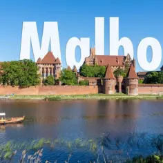Malbork, największy zamek w Polsce, majestatycznie prezentuje się nad rzeką. Statek wycieczkowy płynie spokojnie po wodzie.