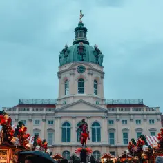 Jarmark świąteczny w Berlinie, z pałacem w tle i ozdobionymi choinkami.