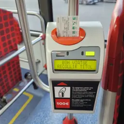 Bilety metro Barcelona w automacie. Na ekranie "BON VIATGE RECOLLIR TITOL". W tle czerwone siedzenia.