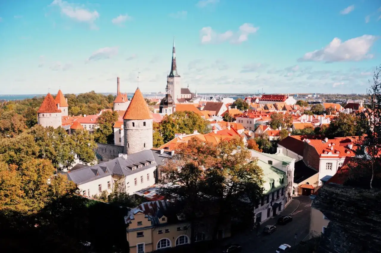Widok na zabytkowe estonia miasta z wieżami obronnymi i czerwonymi dachami, w tle błękitne niebo z chmurami.