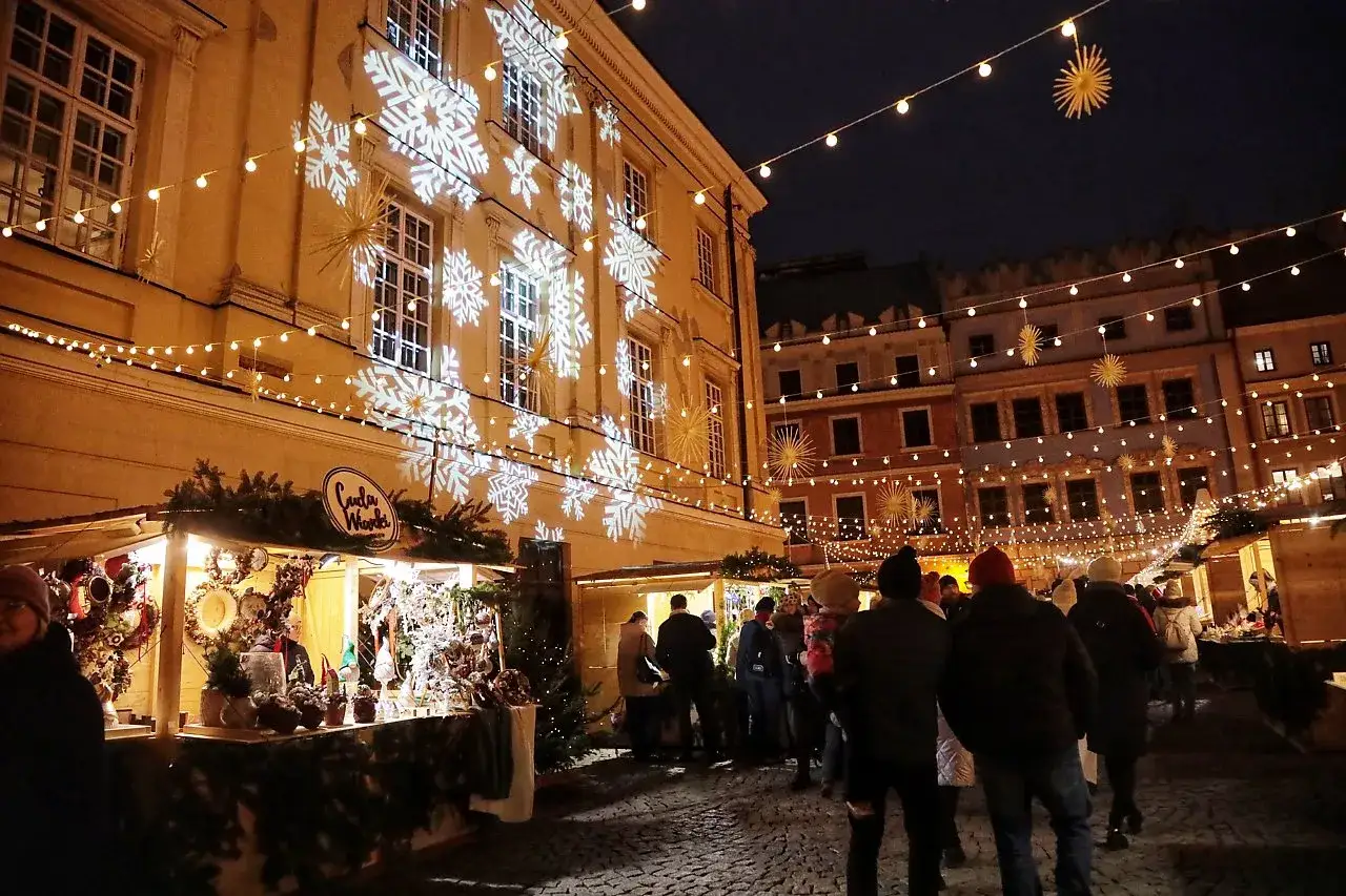 Magiczny jarmark bożonarodzeniowy Lublin nocą. Śnieżynki na budynku, lampki i stragany tworzą świąteczną atmosferę.