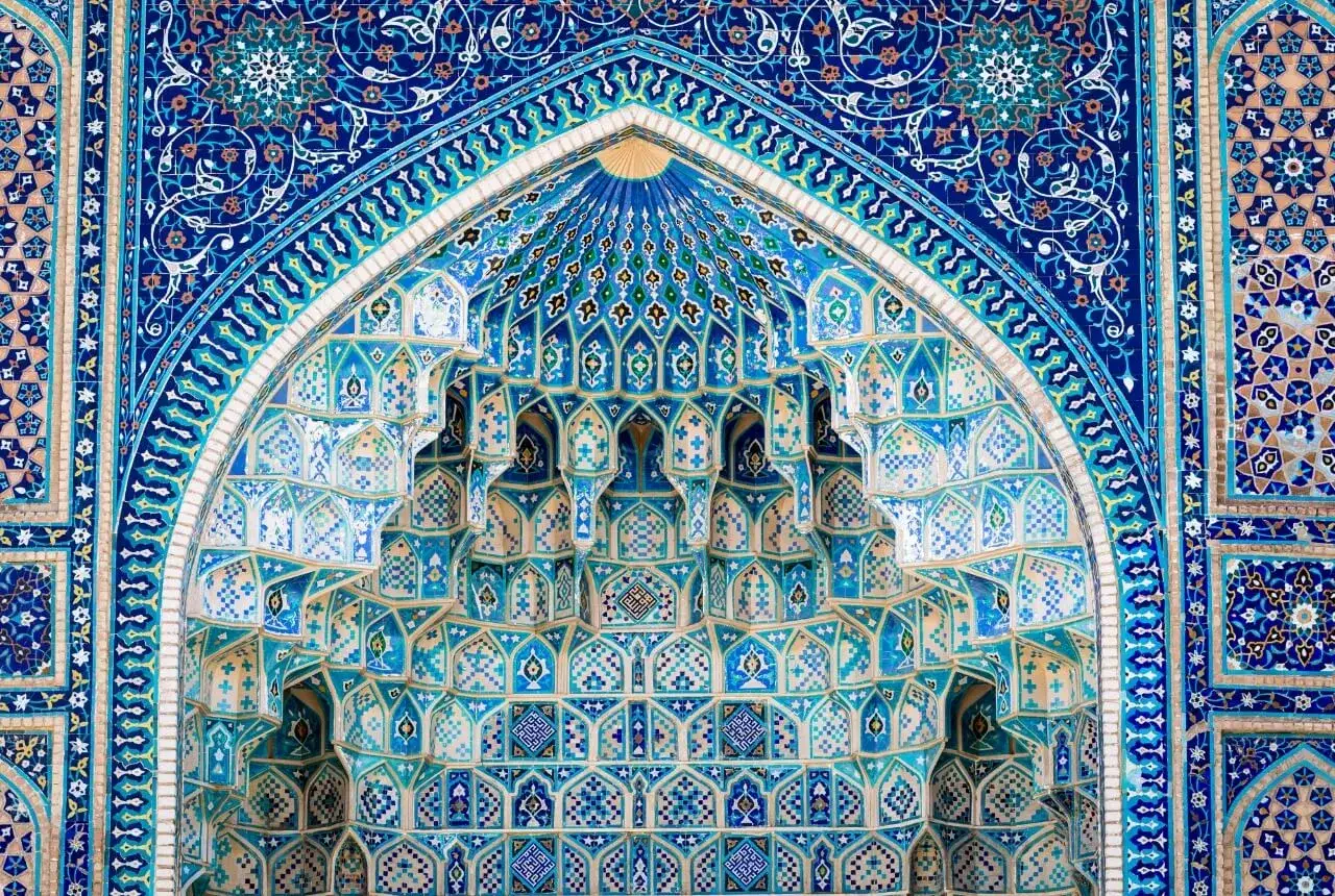Architektura w stylu islamskim z mozaikami w odcieniach błękitu i turkusu. Wzory geometryczne i roślinne zdobią fasadę, przypominając o bogactwie Uzbekistanu, stolicy jedwabnego szlaku.
