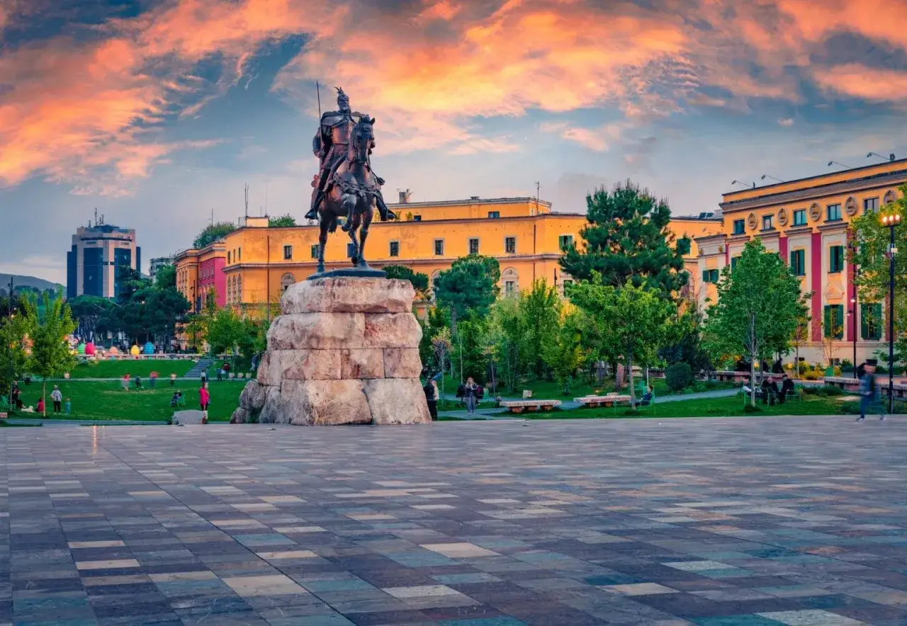 Skanderbeg na koniu, symbol głównego miasta Albanii, na tle kolorowych budynków i zachodzącego słońca.