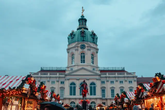 Jarmark świąteczny w Berlinie, z pałacem w tle i ozdobionymi choinkami.